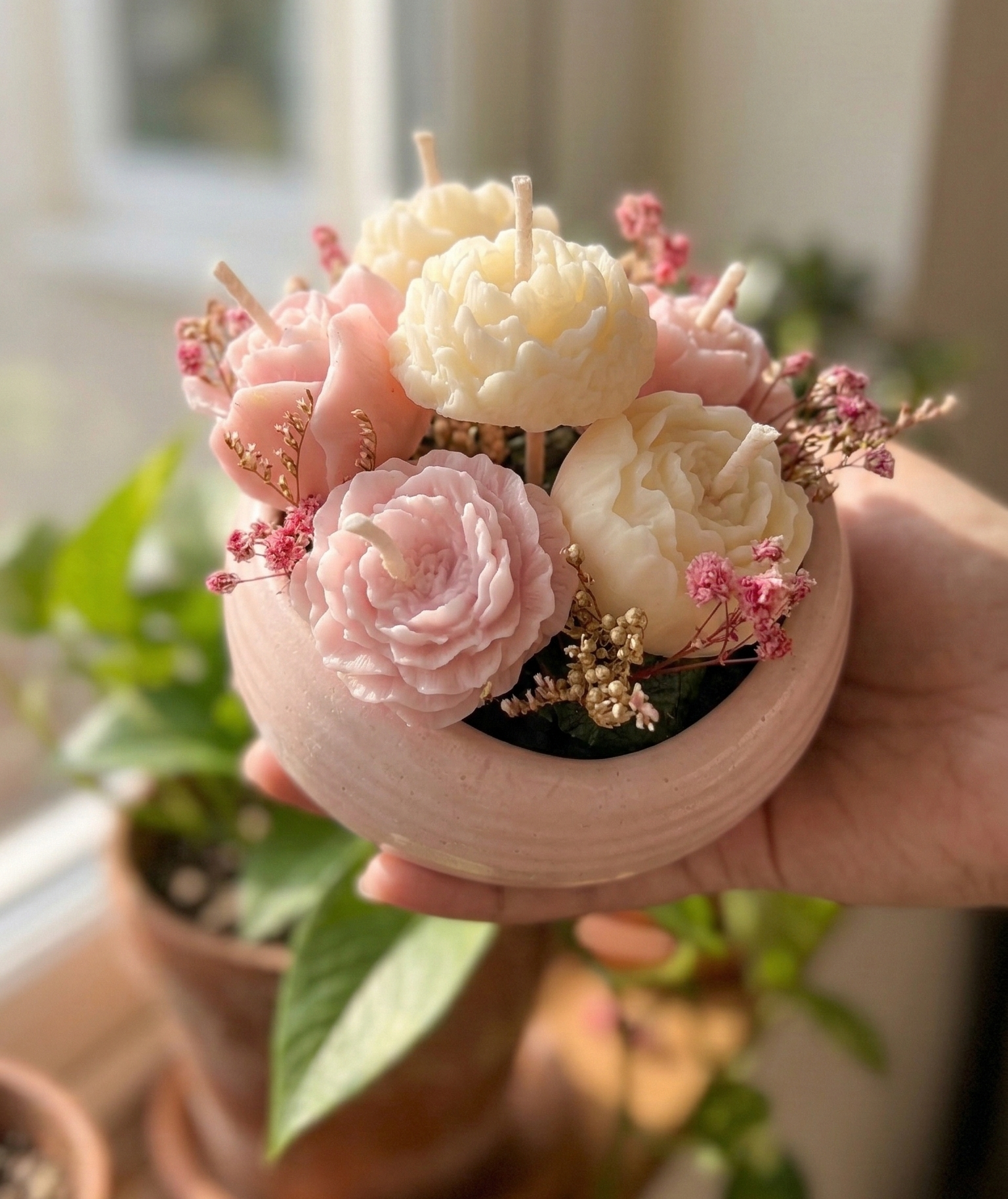 Handmade cream & pink small flowers multi-shaped flower candles in bouquet arranged with dried flowers in a round pink concrete bowl.