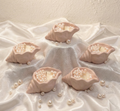 Five handcrafted blush shell candles filled with white wax pearls arranged on a white silk fabric with scattered pearls.