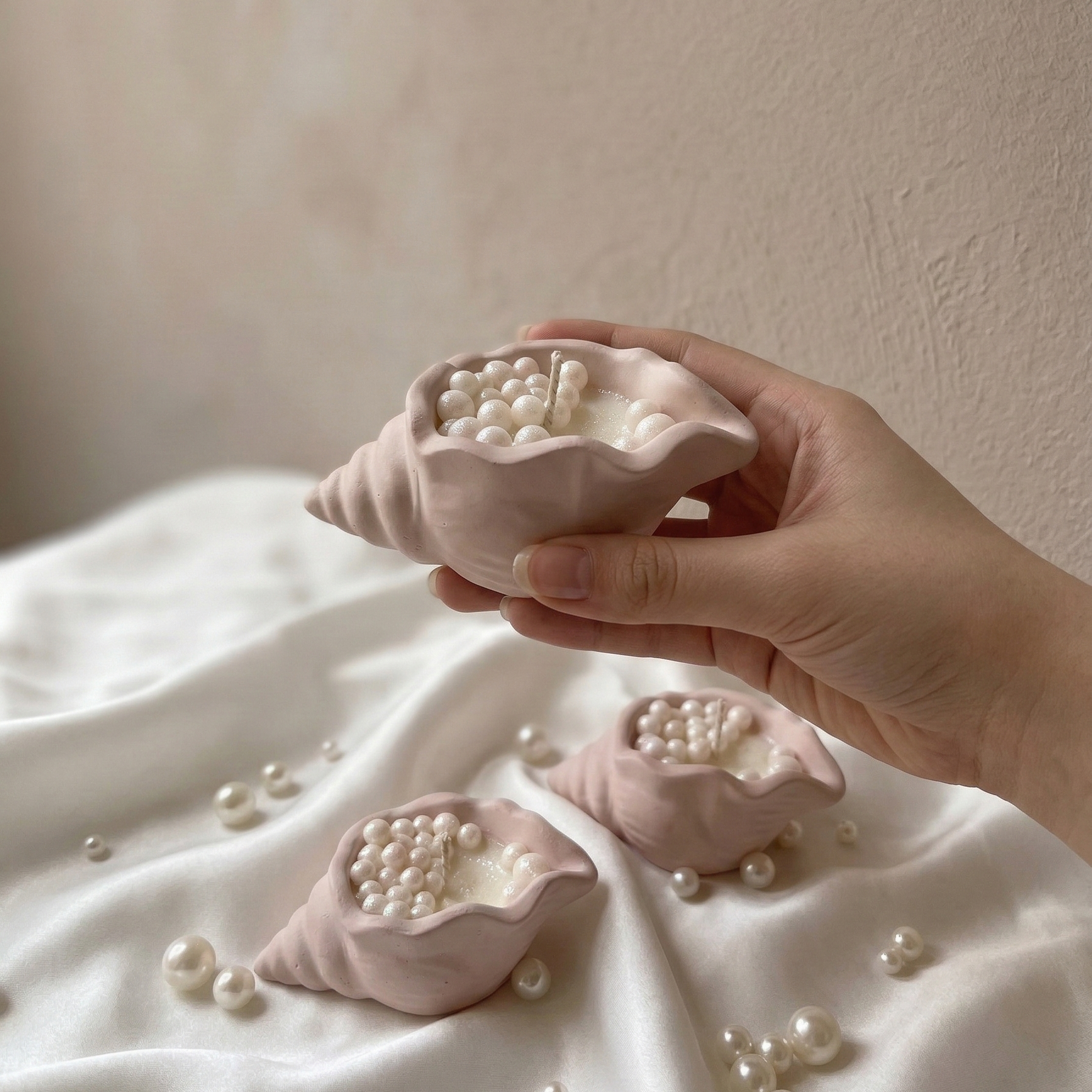 Hand holding a small aesthetic shell candle with shimmering wax pearls, luxury coastal home decor.