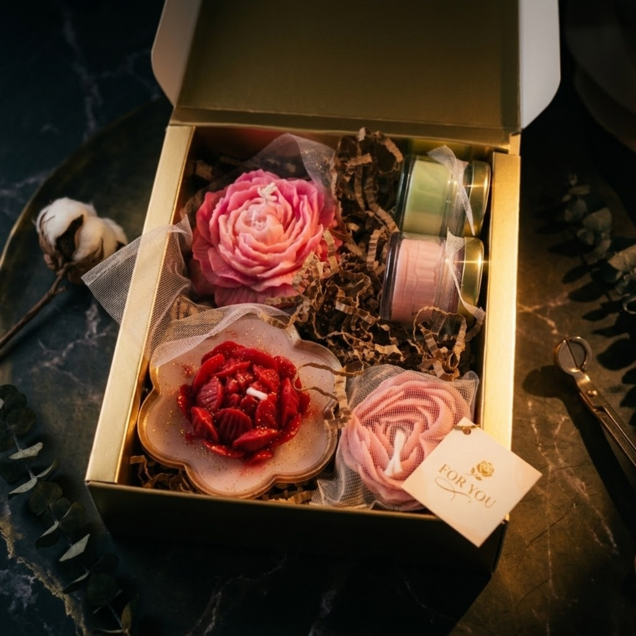 Aesthetic product photography of a floral candle set including a pink peony candle, red lotus bowl candle with gold glitter, heart-shaped rose, and two mini glass jar candles on a dark marble surface