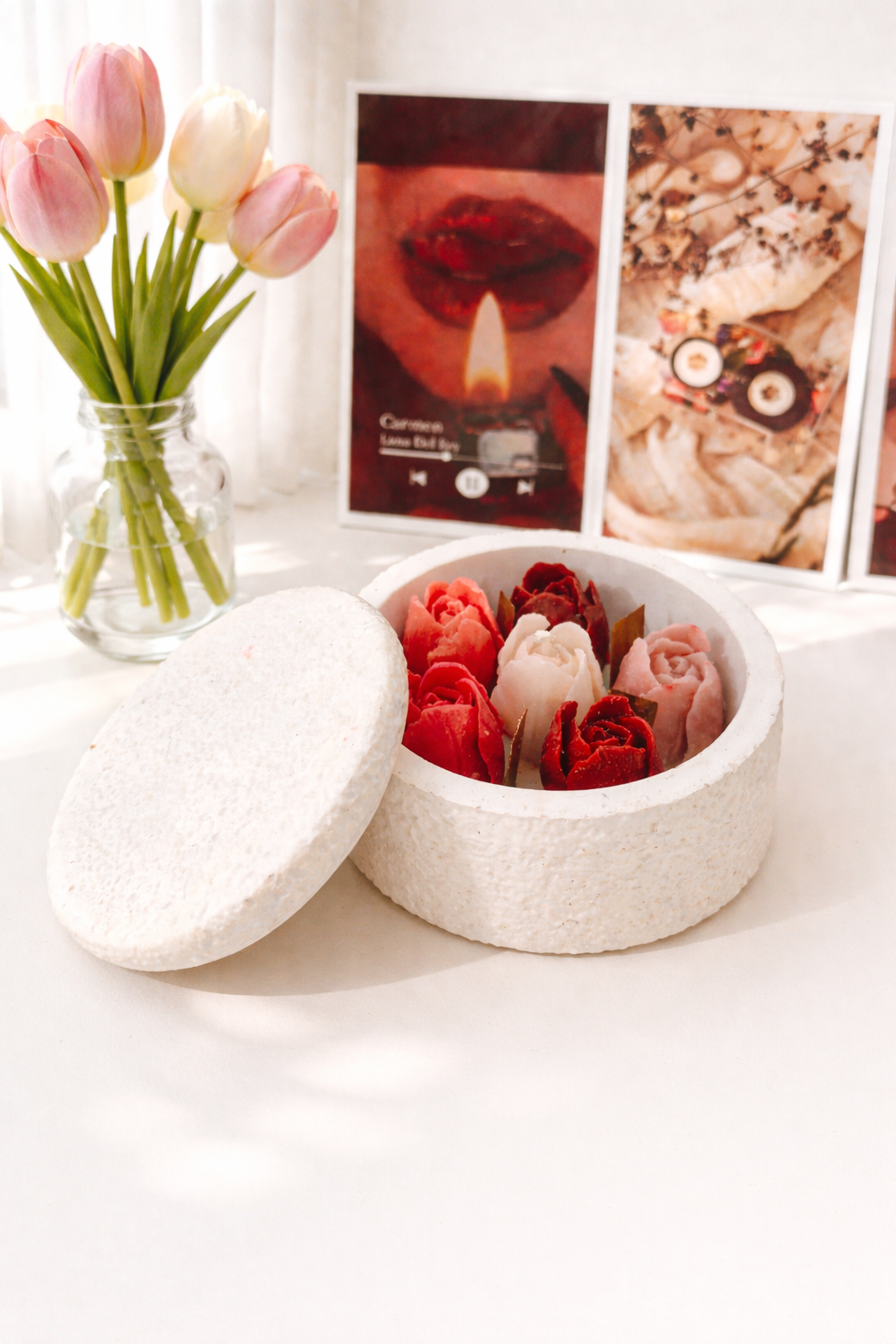 Handcrafted concrete circle candle filled with red and pink wax tulips on a white table next to fresh flowers.