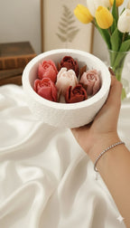 Close-up of a hand holding the Tulip Concrete Circle candle, showing the textured vessel and detailed wax rose and tulip blooms.